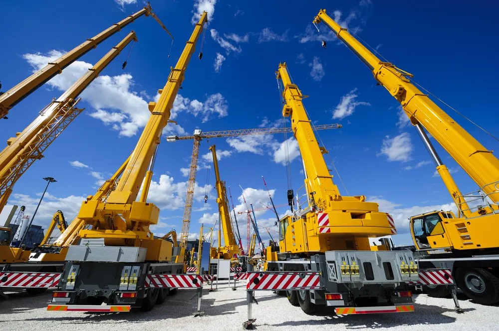 Mobile-construction-cranes-with-yellow-telescopic-arms-and-big-tower-cranes-in-sunny-day-with-white-clouds-and-deep-blue-sky-on-background_result